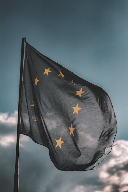 European Union flag gently waving on a flagpole against a cloudy sky, symbolizing unity and patriotism.